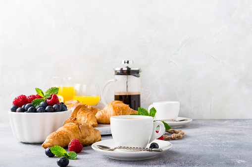 White cups of coffee and croissants on light gray background, selective focus. Healthy breakfast concept with copy space.