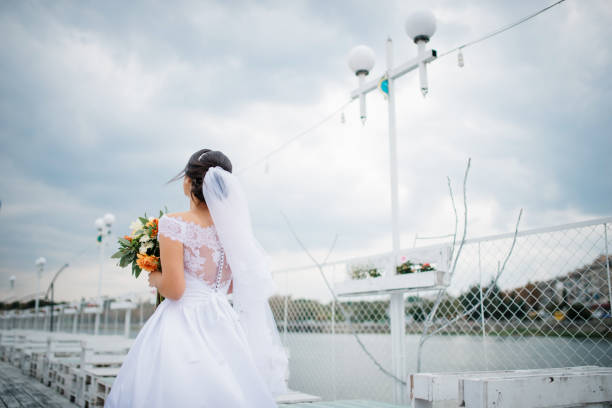 Brunette bride stay on the pier berth at cloudy day.