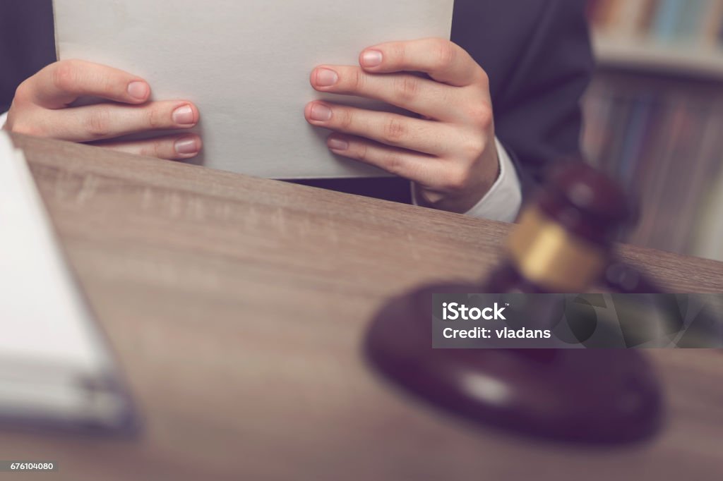 New case Detail of a judge sitting at his desk, holding a file with a new case and studying it. Selective focus Adult Stock Photo