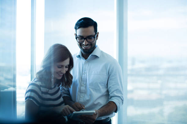 istock Smiling business couple using digital tablet against glass window 676152532