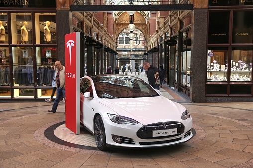 LEEDS, UK - JULY 11, 2016: People walk by Tesla Model S electric car in Leeds, UK. Tesla Motors is one of biggest manufacturers of electric vehicles in the world.