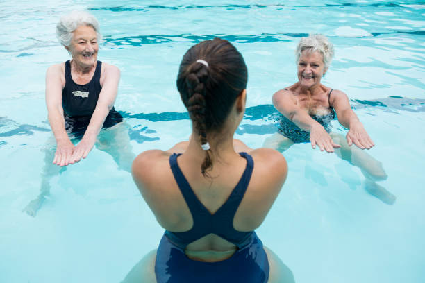 Female trainer with senior women exercising in swimming pool Smiling female trainer with senior women exercising in swimming pool women exercising swimming pool young women stock pictures, royalty-free photos & images