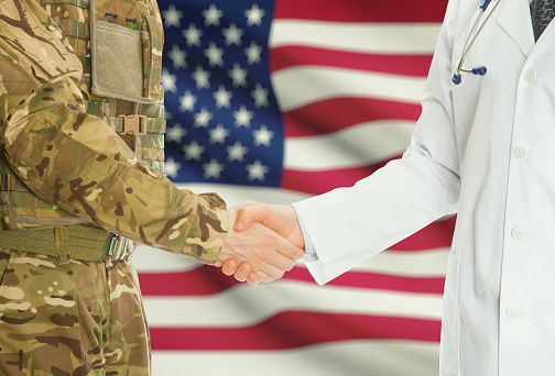 Soldier in uniform and doctor shaking hands with national flag on background - United States