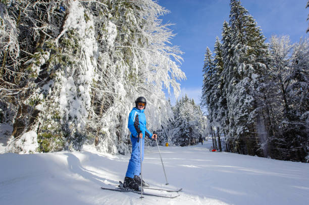 Happy woman skier on a ski slope in the forest Wide low point of view shot of happy woman skier on a ski slope in the forest with big beautiful trees covered in snow. Winter sports concept. Carpathian Mountains, Bukovel bukovel ski resort ukraine stock pictures, royalty-free photos & images