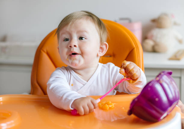 joven niña sucia comiendo en silla alta - baby carrot fotografías e imágenes de stock