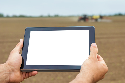 Farmer using tablet computer in agricultural cultivated field. White screen.