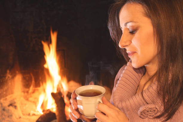 jolie femme buvant une tasse de thé près de l’âtre - feu de cheminée tasse photos et images de collection