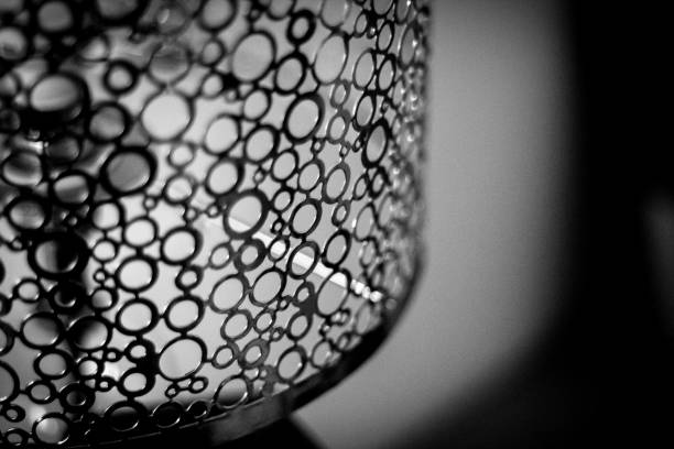 Close up black and white photograph of a metal lamp shade made up of differently sized holes.