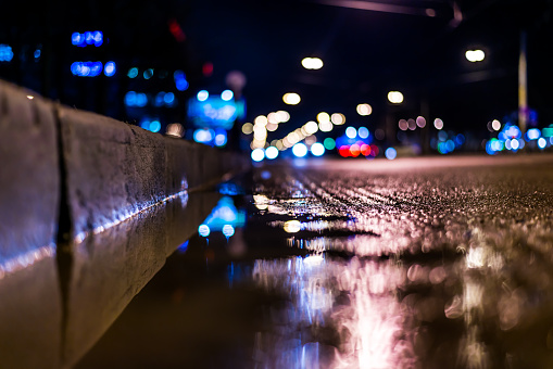 Night city after rain, view of the driving cars from the roadside at the asphalt level, image in the blue tones