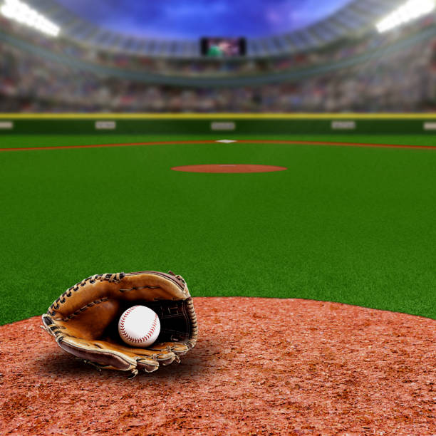 A low angle close-up view of a new baseball in a brown leather baseball glove sitting in the dirt with grass in the background