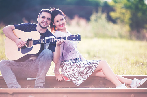 Cute couple sitting on the railroad and posing with a guitar