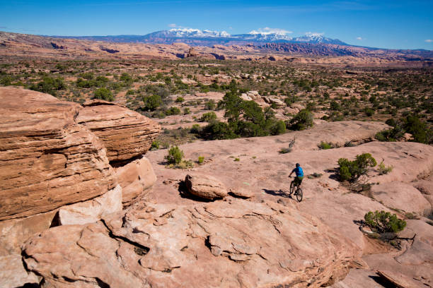 A man rides his mountain bike on a cross-country trail in Moab, Utah, USA on a sunny day. In the background are the snow-covered La Sal Mountains. la sal mountains stock pictures, royalty-free photos & images