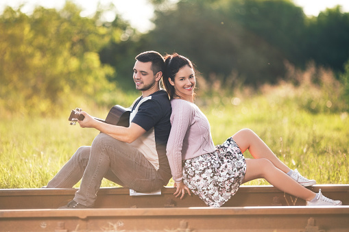 Cute couple with a guitar sitting on the railroad in a spting time