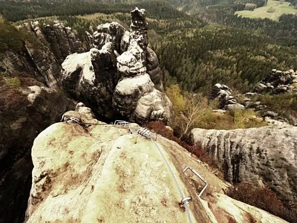 Photo of Climbers ladder. Iron twisted rope fixed in block by screws snap hooks. The rope end anchored into sandstone rock.