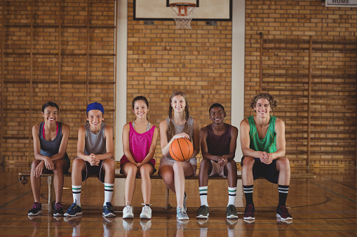 Portrait of high school kids sitting on a bench in basketball court