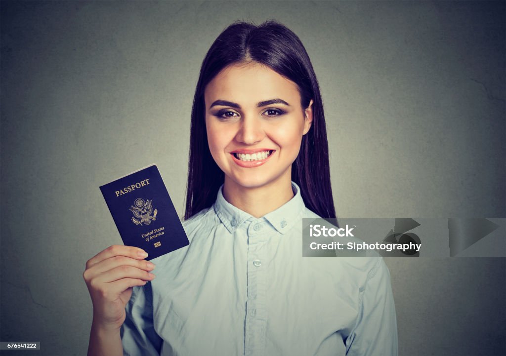 Attractive young happy woman with USA passport Portrait attractive young happy woman with USA passport isolated on gray wall background. Positive human emotions face expression. Immigration travel concept Adult Stock Photo