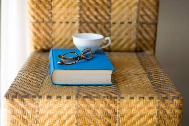 Blue book, white cup and eyeglasses on a chair.
