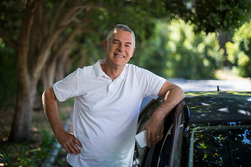 Portrait of smiling senior man standing by car