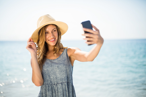 Young woman smiling while taking selfie against sea on sunny day