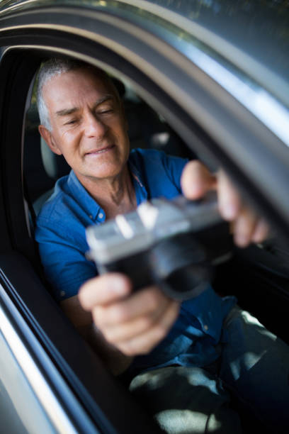 istock Senior man taking selfie with camera while sitting in car 676597364