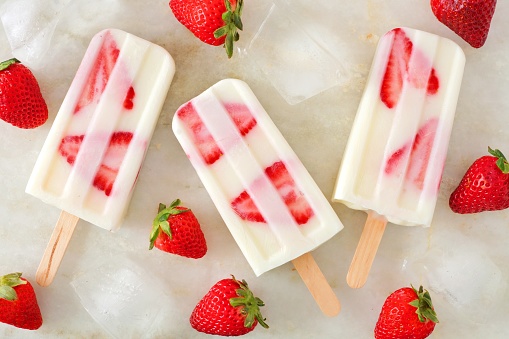 Healthy strawberry yogurt popsicles, overhead view on a marble background