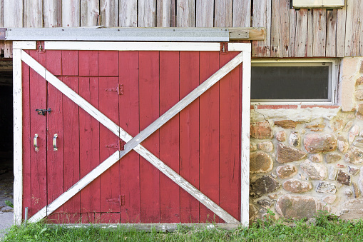 Partially open red barn door in a weathered barn.  Traditional white framing, weathered wood, field stone, texture and nostalgia.