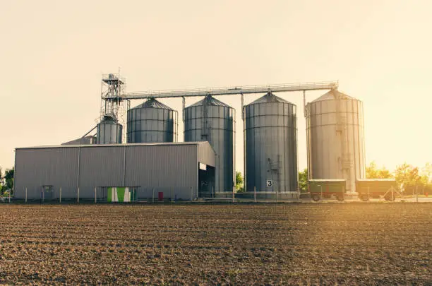 Agricultural silos on sunset and part of field and fertile soil in foreground