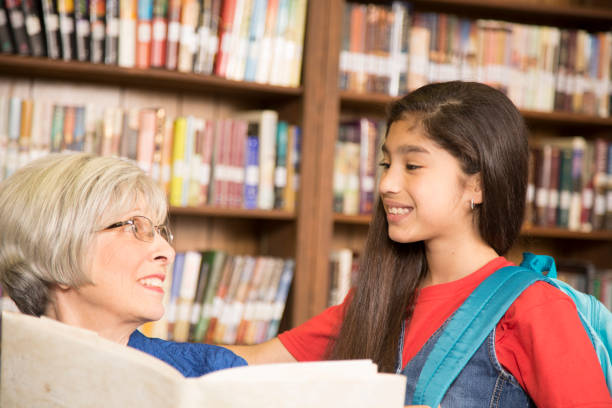 istock Teacher, librarian reads book to elementary student in library or classroom. 676648212