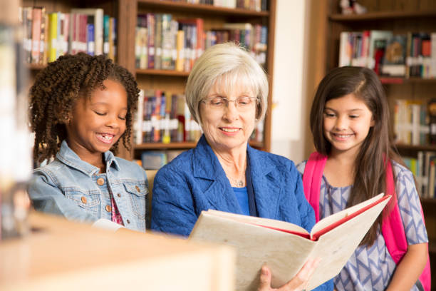 istock Teacher, librarian reads book to elementary students in library or classroom. 676657404