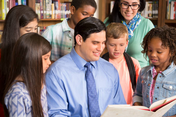 istock Teacher, librarian reads book to elementary students in library or classroom. 676668608