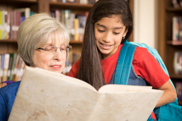 istock Teacher, librarian reads book to elementary student in library or classroom. 676674466
