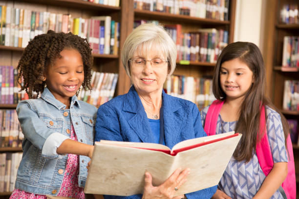 istock Teacher, librarian reads book to elementary students in library or classroom. 676681162