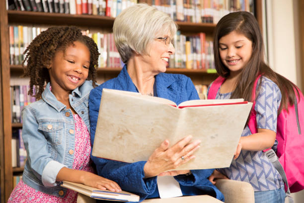 istock Teacher, librarian reads book to elementary students in library or classroom. 676692760