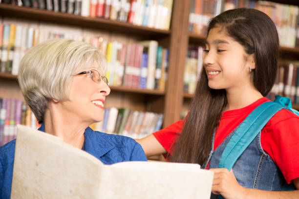 istock Teacher, librarian reads book to elementary student in library or classroom. 676705894