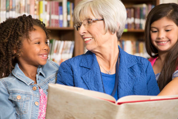 istock Teacher, librarian reads book to elementary students in library or classroom. 676715382