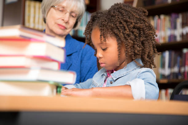 istock Teacher, mentor helps elementary-age schoolgirl with homework. 676716128