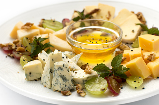 Four kinds of cheese, decorated with grapes, walnuts, mint and honey. All on a white plate on a white, isolated background.
