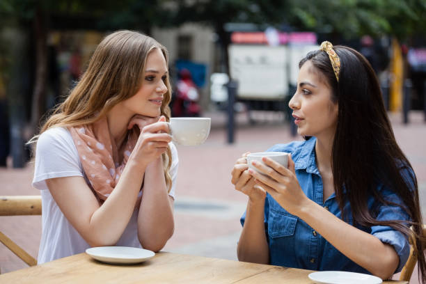 friends drinking coffee while sitting at sidewalk cafe - front view cup saucer white imagens e fotografias de stock