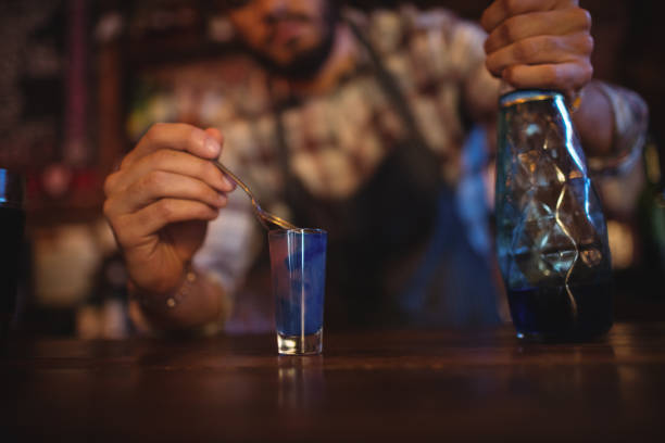 Waiter pouring cocktail drink into shot glasses at counter