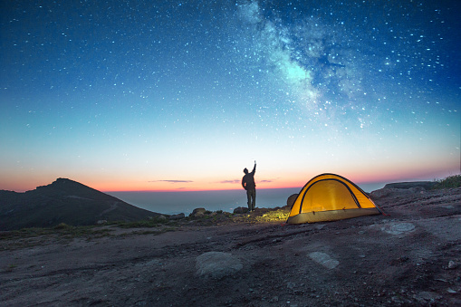 one man camping at night with phone into the sky