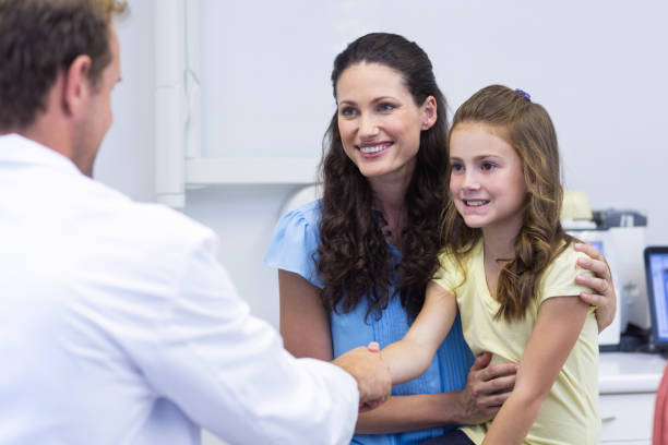 Dentist shaking hand with daughter after dental examination