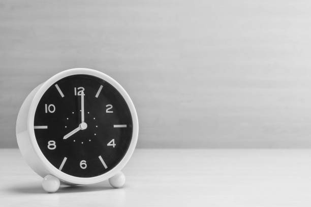 despertador de primer plano para decorar en 8:00 en el escritorio de madera y fondo de textura de la pared en tono blanco y negro con espacio de copia - 8 oclock fotografías e imágenes de stock