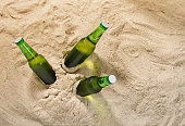 istock Three bottles of cold light beer on sand with copy space, top view 677193544