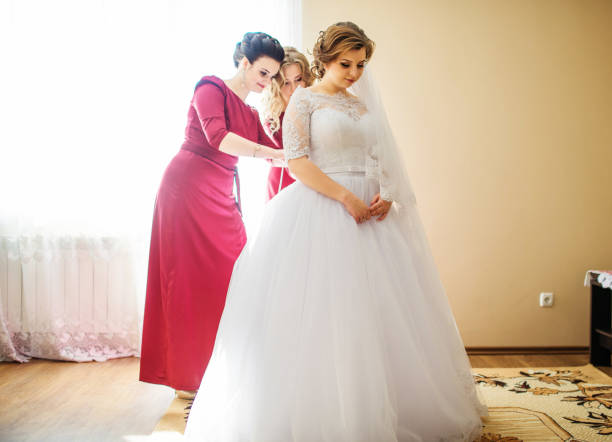 istock Bridesmaid in red dresses help bride to dressed wedding dress. 677274104