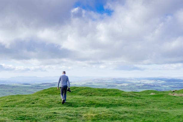 istock man walking with camera on a hillside with countryside views. 677327312