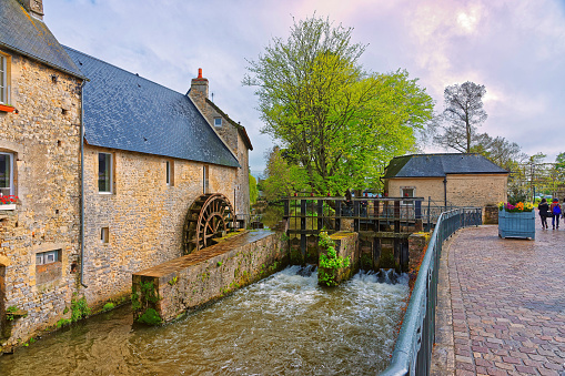 Bayeux, France - May 8, 2012: Water mill and Aure River in the old city of Bayeux in Calvados department in Normandy, France. People on the background