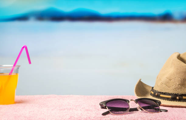istock Summer holiday background with free empty blank copy space. Brimmed hat, sunglasses and yellow drink on towel in paradise lagoon beach with blue water and sky. Promotion template for spring discount. 677376628