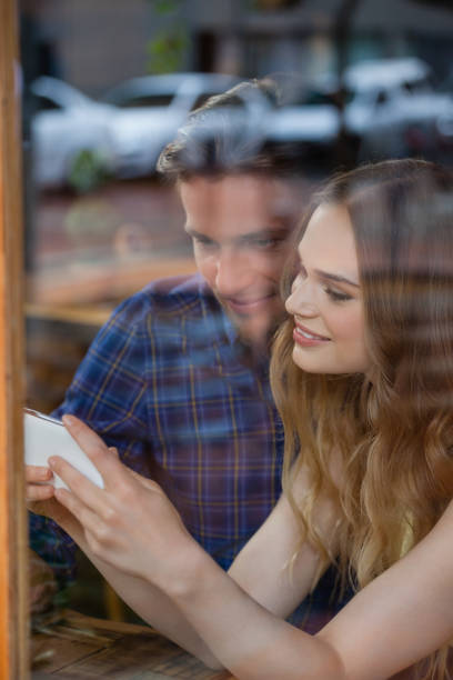 istock Happy couple holding smart phone while sitting at cafe 677378356