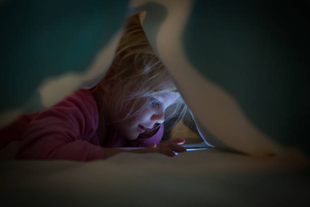 istock Little girl on cell phone under duvet 677444442