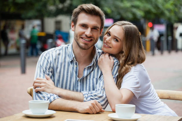 portrait of happy couple sitting at sidewalk cafe - front view cup saucer white imagens e fotografias de stock